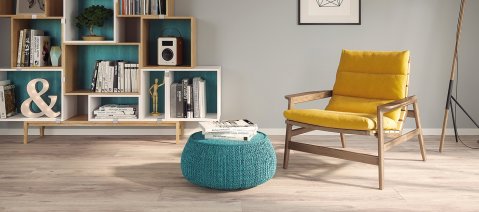 wineo Laminatboden im Wohnzimmer mit einem gelben Stuhl, einem türkisen Hocker und Bücherregal