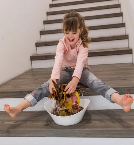 wineo Treppenkante Kind auf Treppe spielt mit Laub nass barfuß